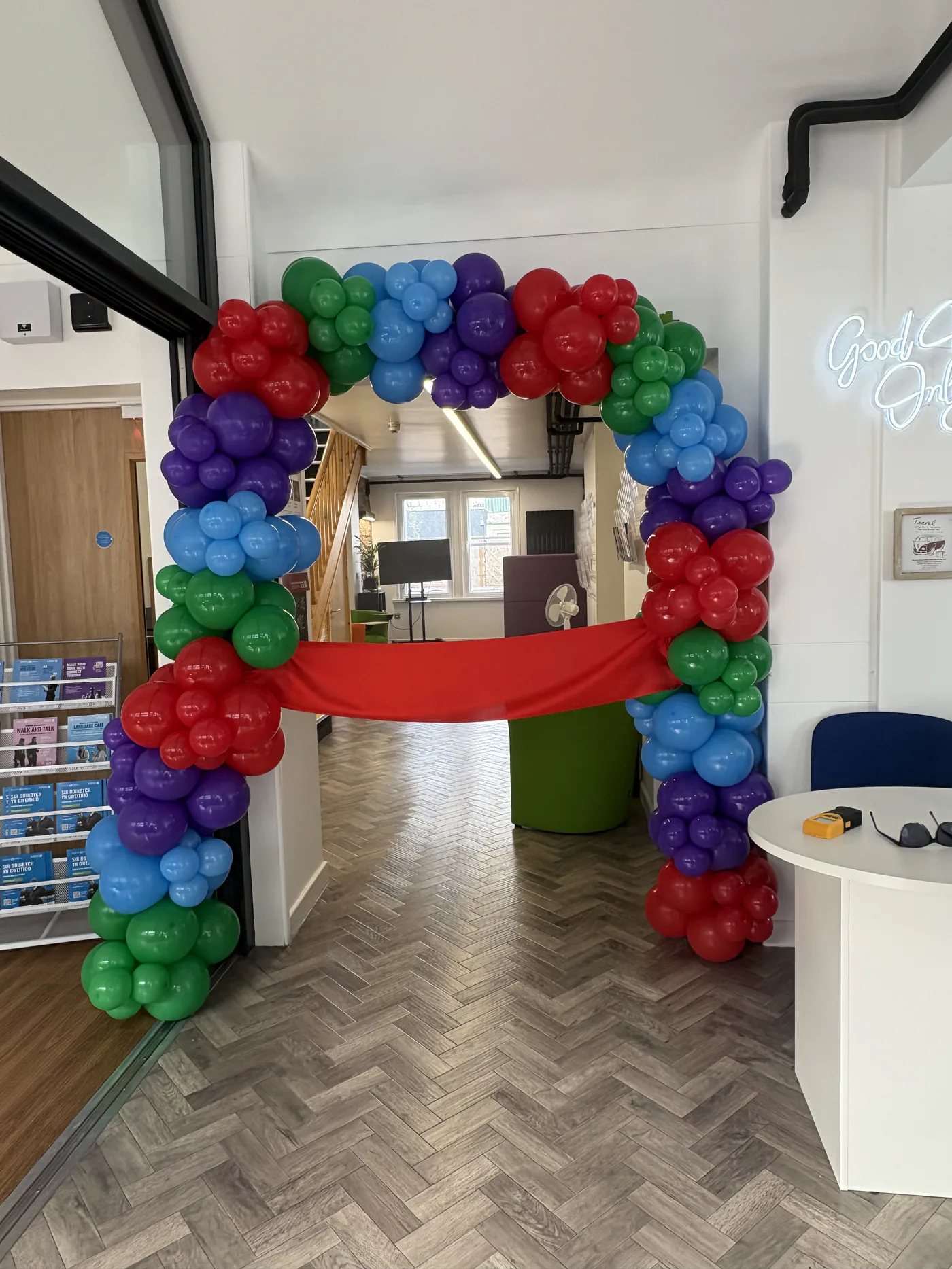 A full balloon arch in red, blue, green and purple framing a business entrance, with a ribbon stretched across ready to be cut.