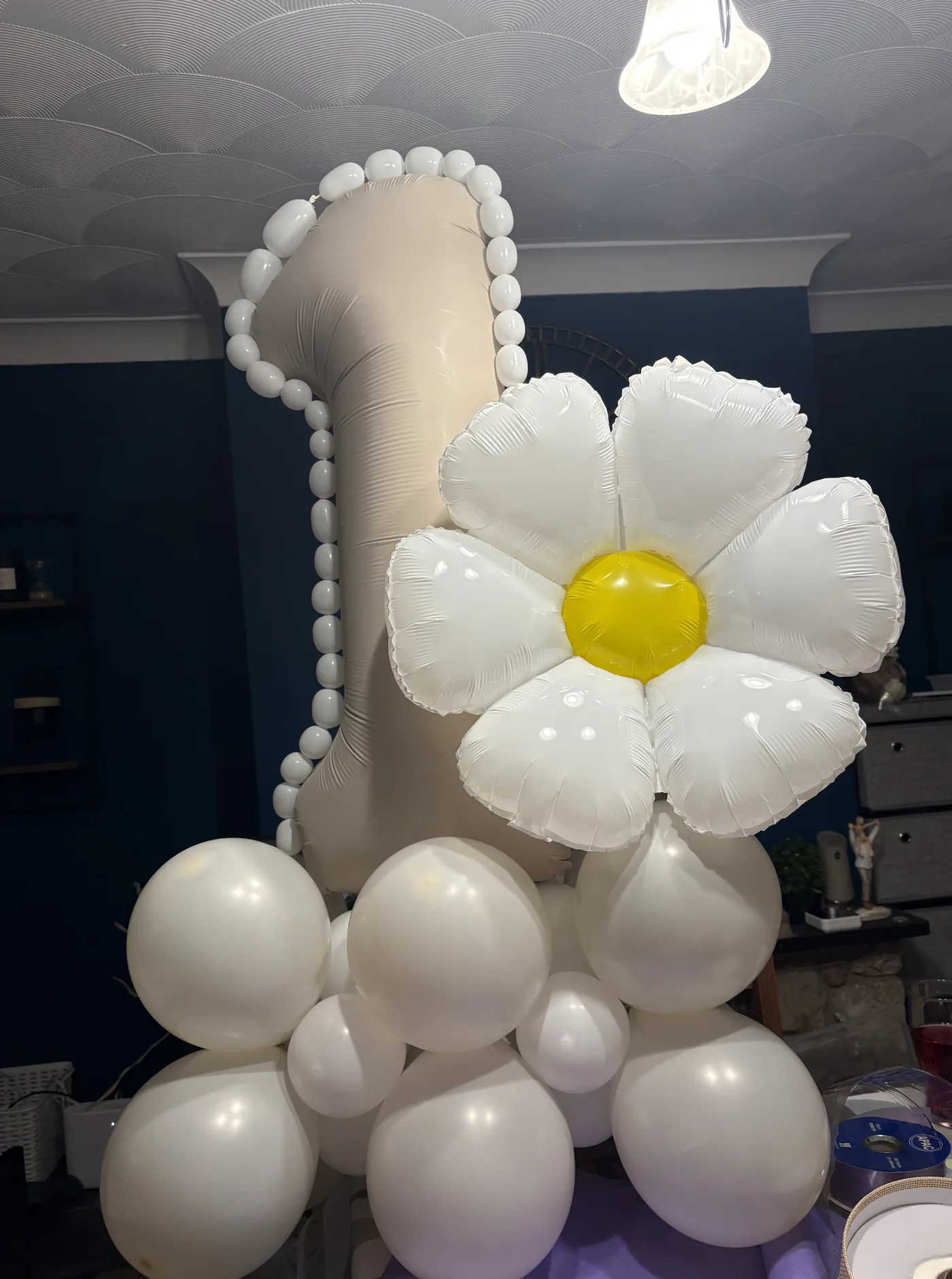 A first birthday display built around a tall number one balloon, an oversized daisy, and a base of white balloons.