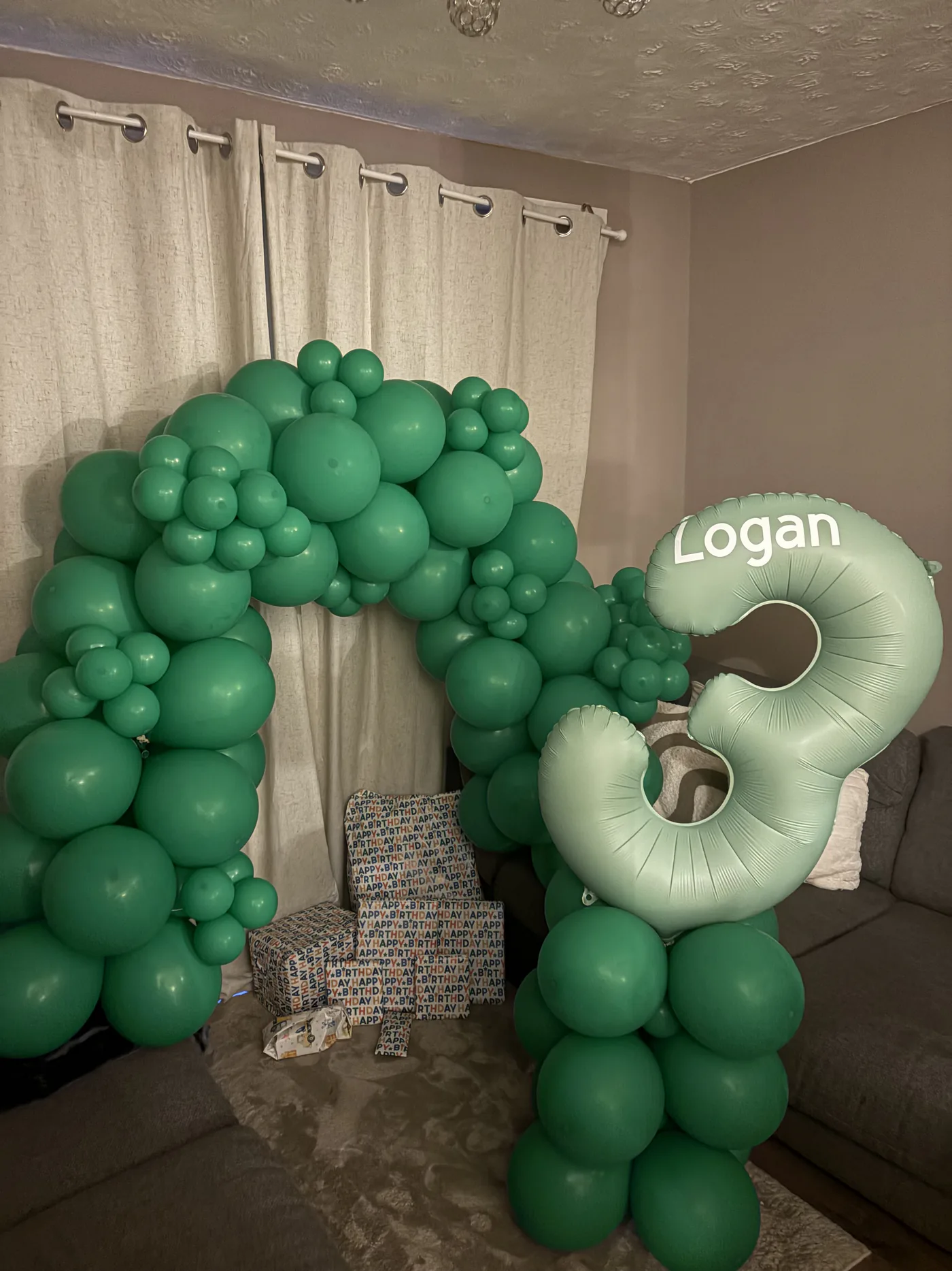 A hand-built balloon arch in shades of green, paired with a personalised foil number balloon.