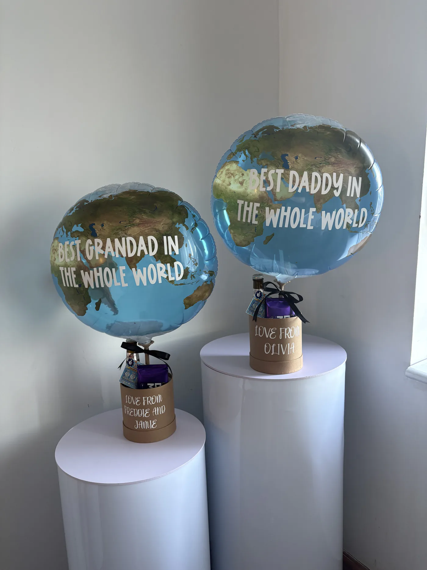 Two personalised globe foil balloons mounted on gift boxes and displayed on white plinths.